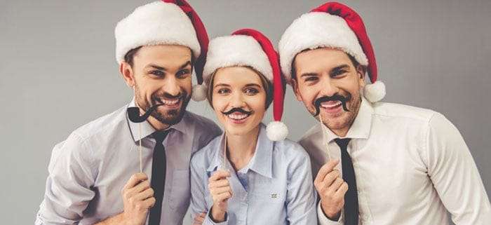 Karriere auf Weihnachtsfeier fördern drei Mitarbeiter vor Fotobox und mit Weihnachtsmützen
