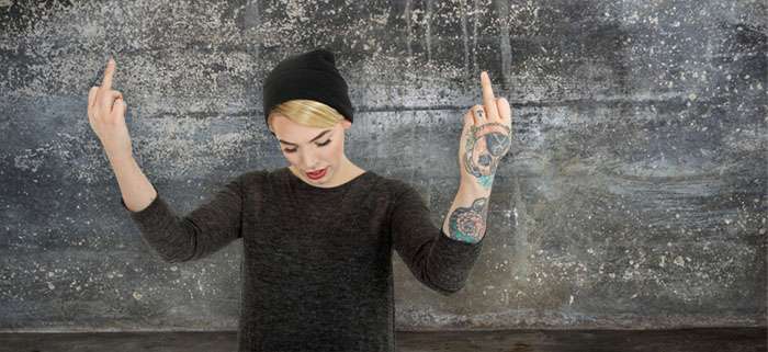 Blondes Mädchen mit Mütze und Tattoo zeigt beide Stinkefinger